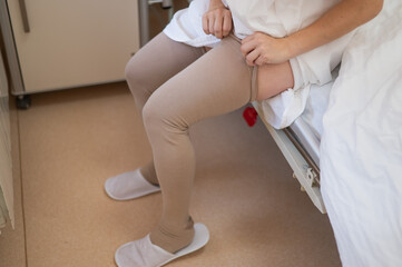 A woman puts on post-operative compression stockings in a hospital room. 