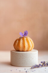 Lavender-infused madeleine with honey glaze on a speckled beige pedestal and earthy tones background, creative pastry food styling
