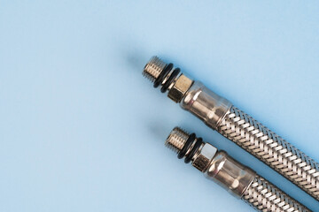 Braided stainless steel plumbing hoses with threaded connectors isolated on the blue background.