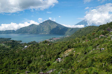 Fototapeta premium Serene lake surrounded by lush green mountains and blue skies, offering a breathtaking panoramic view.