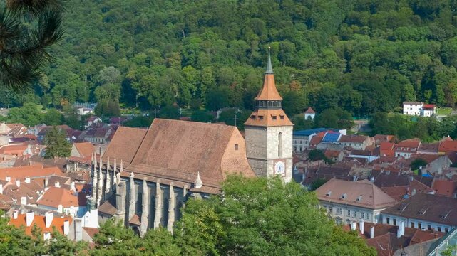 Brasov cityscape showcasing black church, council square, and surrounding red-roofed buildings, nestled amidst lush greenery