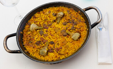 Delicious Spanish paella in traditional paellera, featuring rich mix of rice, saffron, various meats, mushrooms and artichokes, perfect for hearty meal