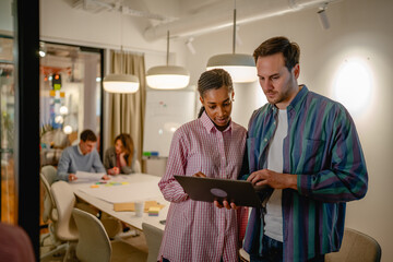 two diverse male and female colleague use laptop at office