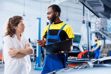 Mechanic in car service uses laptop to calculate invoice after fixing broken automobile fuel tank....