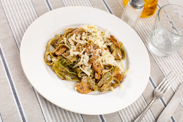 Hearty and simple homemade lunch. Italian past with mushrooms, dish is sprinkled with grated cheese. Cutlery and glass for drinks are prepared for meal.
