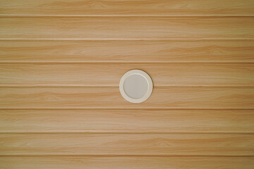 A round, recessed lighting fixture is mounted on a light brown wood paneled ceiling. The overall look is clean and modern.Recessed Lighting Fixture on Light Brown Wood Paneling Ceiling