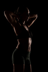Silhouette of a Fit Woman in Gymwear Posing Against a Dark Background with Dramatic Lighting