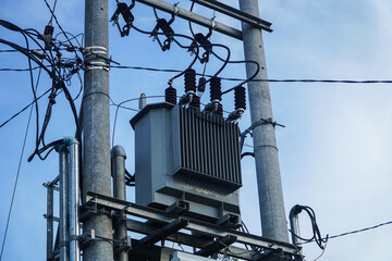 Close-up of a power transformer mounted on a utility pole. The wires and cables are visible against...