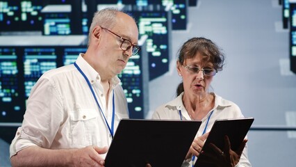 Data storage company executives looking around data center, using laptop and tablet to crosscheck contingency plan and assess high tech workspace units in need of fixing, preventing liabilities