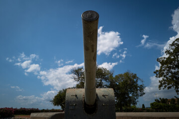A weathered cannon points towards a bright, partly cloudy sky, surrounded by tranquil greenery.