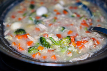 A creamy chicken and vegetable soup, simmering in a wok. The soup is rich with carrots, broccoli, and hard-boiled eggs. Creamy Chicken and Vegetable Soup in a Wok