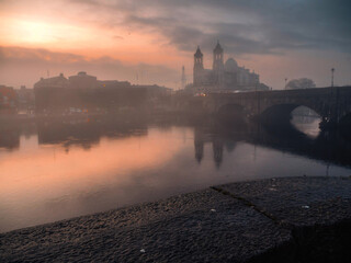 View on Church of Saints Peter and Paul at dusk. Warm color light. Cloudy sky reflects in river...
