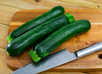 There are several pieces of zucchini on cutting board, with dark green peel. Ripe vegetables, process of preparing vegetables for baking and stewing