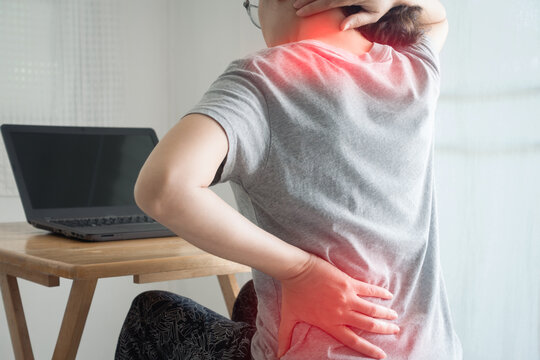 Office syndrome concept. Young woman suffering from office syndrome having lower back pain, neck and shoulder pain sitting on chair at home. Female feeling pain in neck after work on laptop long time.
