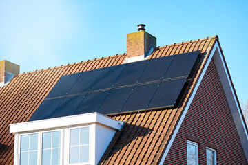 Solar panels on red tile roof, blue sky background, sunny day, close up