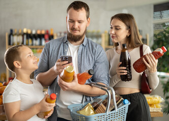 Family choose bottles of juice and scan QR code with smartphone in supermarket