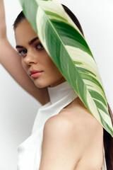 Elegant young woman with a leaf posing against a light background, showcasing natural beauty and modern fashion style.