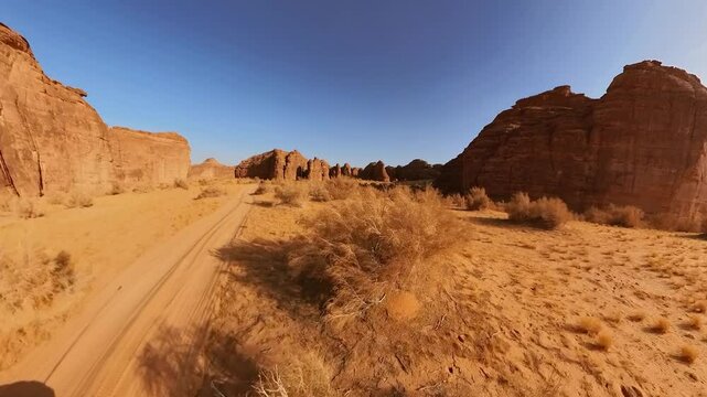 Aerial view on off road vehicle driving through the desert landscape of Alula Sharaan Nature Reserve in Saudi Arabia, featuring sandstone mountains and sparse vegetation under a clear blue sky