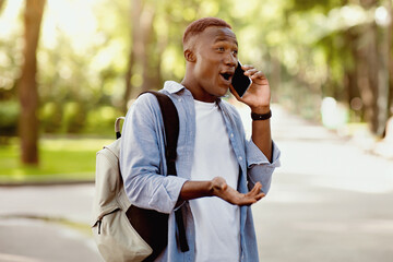 Surprised black guy having conversation on mobile phone at park. Handsome African American man...
