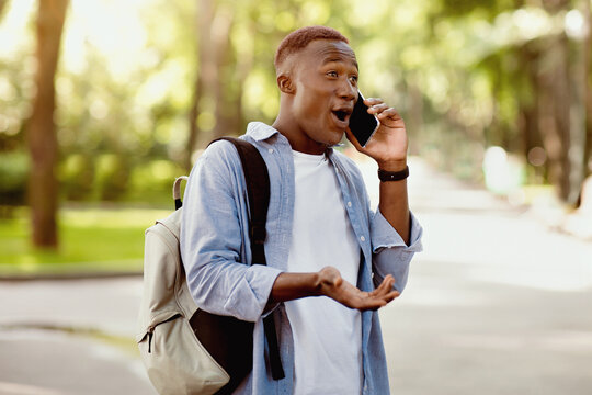 Surprised black guy having conversation on mobile phone at park. Handsome African American man shocked over hearing unexpected news, excited to talk to good friend or family - Powered by Adobe