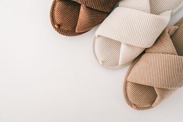 Three pairs of ribbed fabric slippers in neutral tones—beige, white, and brown—are arranged on a clean white background. The minimalist and cozy design emphasizes comfort and modern home aesthetics