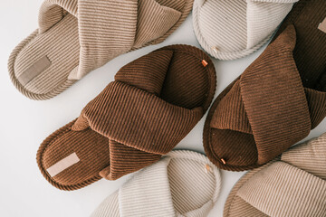Three pairs of ribbed fabric slippers in neutral tones-beige, white, and brown-are arranged on a...