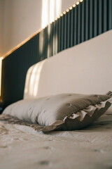 A soft decorative pillow with ruffled edges resting on a neatly made bed, illuminated by warm...