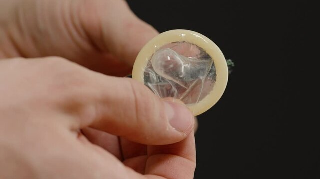 Hands Holding a Condom and Carefully Removing It from Its Packaging, Highlighting Preparation for Safe and Responsible Use