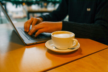 Man working on a laptop in a cozy cafe with a cup of coffee on the wooden table, warm lighting creating a relaxed atmosphere