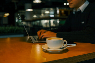 Man working on a laptop in a cozy cafe with a cup of coffee on the wooden table, warm lighting creating a relaxed atmosphere