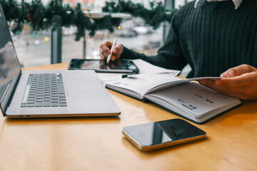 A professional workspace with a person organizing tasks using a notebook, tablet, and laptop on a wooden table, creating a productive and modern office environment