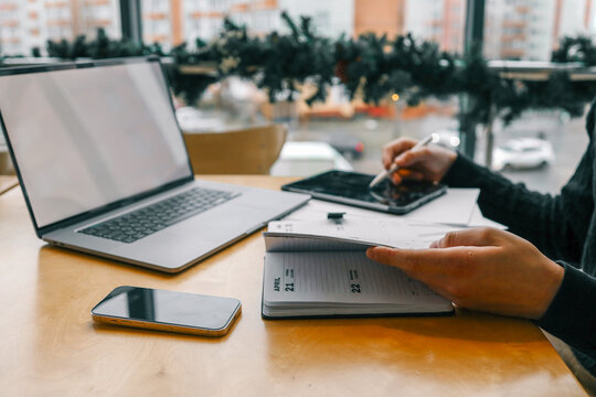 A professional workspace with a person organizing tasks using a notebook, tablet, and laptop on a wooden table, creating a productive and modern office environment