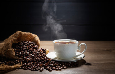 Hot coffee in a white coffee cup With roasted coffee beans on a wooden table, dark black background.