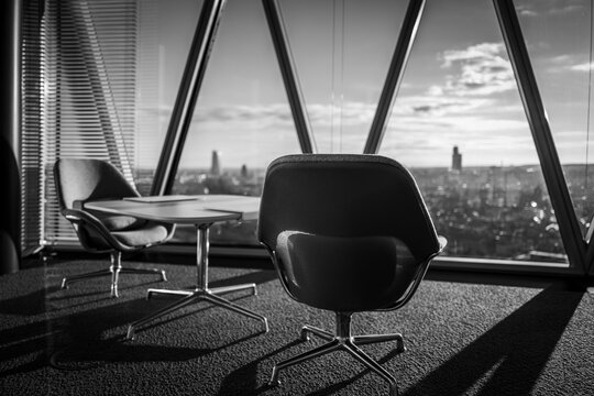 A modern office boasts a stunning city view, with sleek chairs and a minimalist table near panoramic windows.