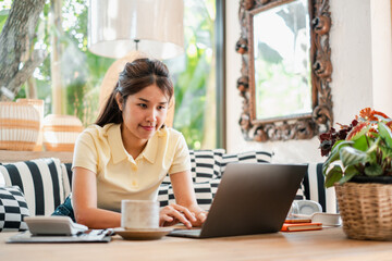 A young woman focused on her laptop in a cozy, well-decorated living room with natural light and modern furnishings.