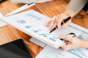 Close-up of hands reviewing marketing report with charts and graphs on a clipboard, highlighting...