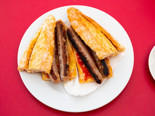 Bologna sandwich served on white circular plate with serving pieces.