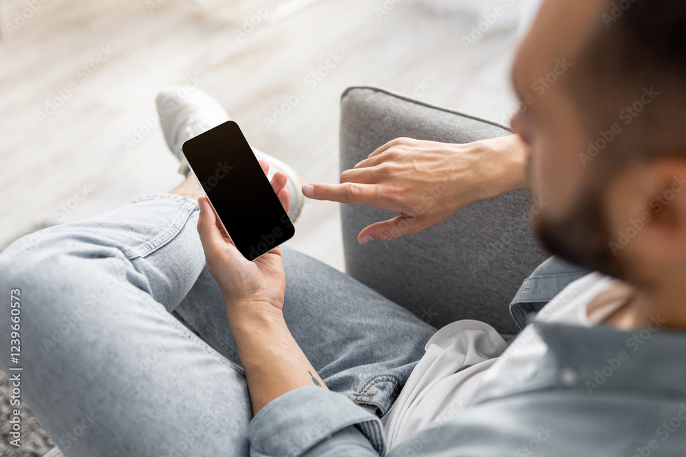 Poster unrecognizable young guy using smartphone with empty screen at home, mockup for website or mobile ap