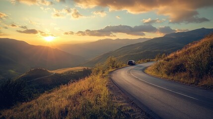 A small car winds along a mountain road, with a breathtaking view of the landscape bathed in the warm glow of the setting sun, creating a picturesque scene.