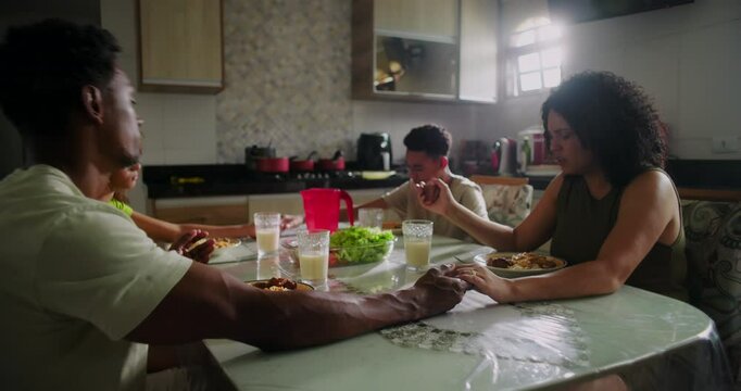 Family praying together and then starting to eat the meal at the dining table, symbolizing gratitude, spirituality, and togetherness in a warm and intimate home setting