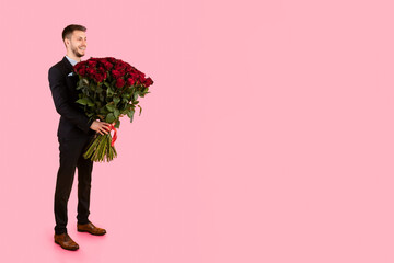 Boyfriend Holding Huge Bouquet Of Red Roses Standing Over Yellow Studio Background, Wearing Elegant Suit. Romantic Date Concept