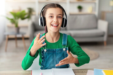 Portrait of smiling girl wearing wireless headphones talking and gesturing, looking at camera,...