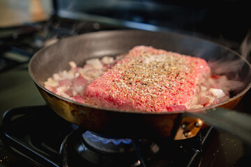 Square of ground meat in a skillet starting to cook 