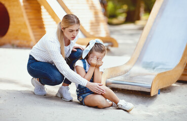 Playground Injury. Mother Examining Daughter's Injured Knee After Ride On Dangerous Slide In Park.