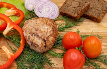 Fried chicken cutlet on a wooden tray with cherry tomatoes, rings of pepper, onion, herbs and pieces of black bread. Homemade food. healthy lifestyle concept.