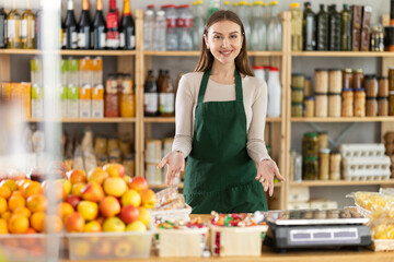 Positive young saleswoman is standing at the counter ready to welcome customers in grocery store