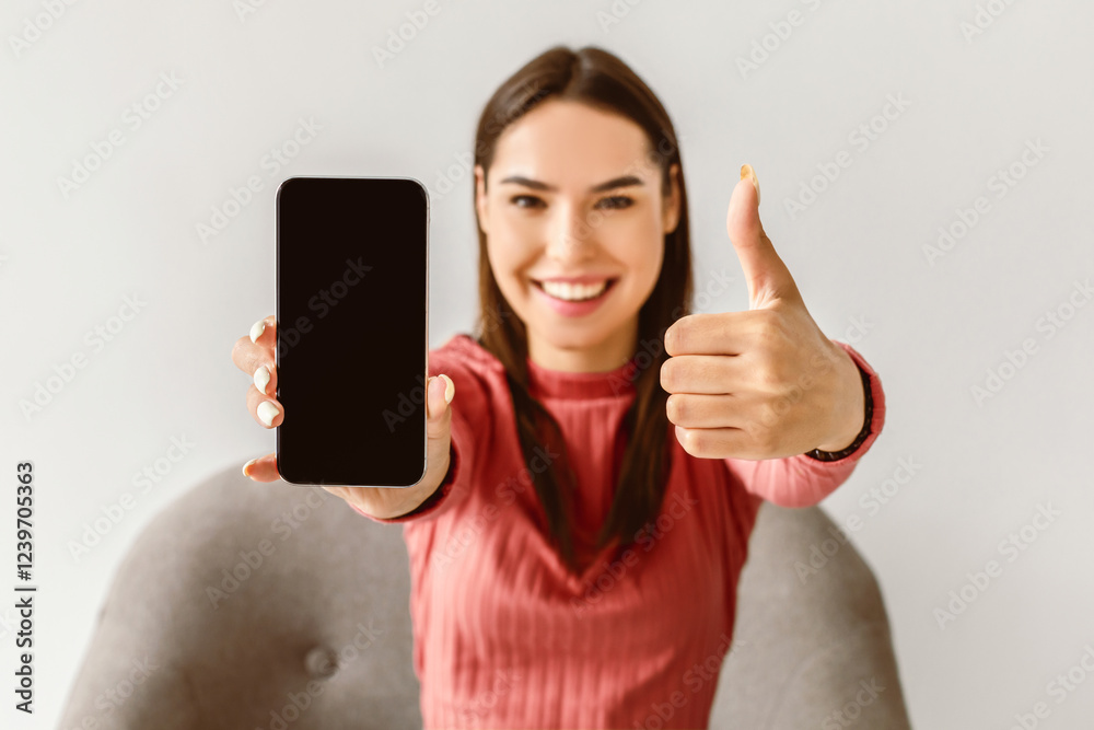 Poster Happy Caucasian lady showing cellphone with empty screen and gesturing thumb up, recommending new mobile app or website on white studio background, mockup for advertisement