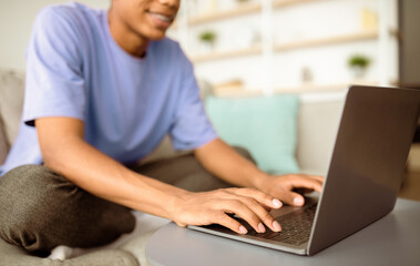 E-learning concept. African American adolescent studying online, typing on laptop at home, closeup of hands. Black teenager using PC to make homework, communicate to teacher on webcam