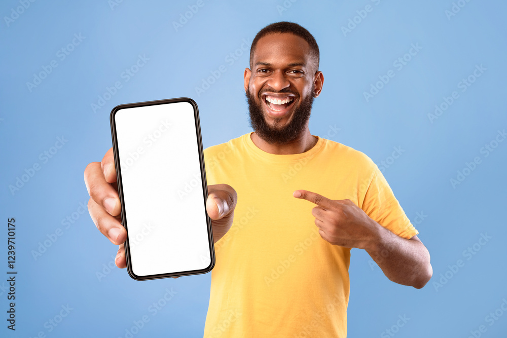 Poster handsome happy african american guy pointing at smartphone with blank screen on blue studio backgrou