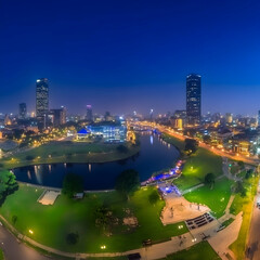 Fototapeta premium Cityscape at Night: Illuminated Buildings, River, and Park in Tranquil Twilight